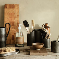 Matte black and earthy brown kitchen utensils and decor arranged on a rustic wooden surface, featuring natural textures.