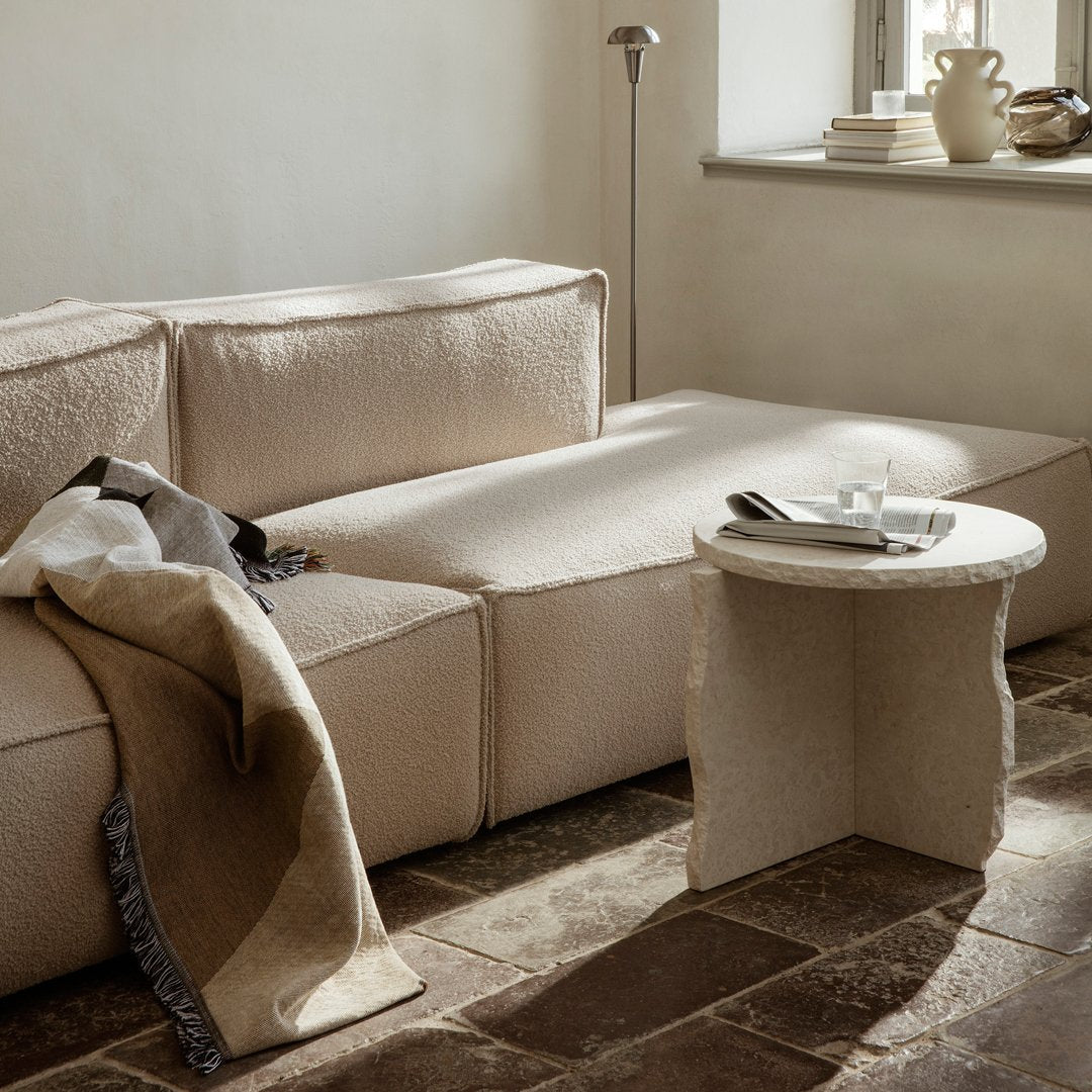 Elegant beige sofa with textured fabric and a soft, neutral throw blanket draped over. Warm earthy tones throughout.