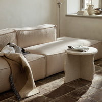 Elegant beige sofa with textured fabric and a soft, neutral throw blanket draped over. Warm earthy tones throughout.