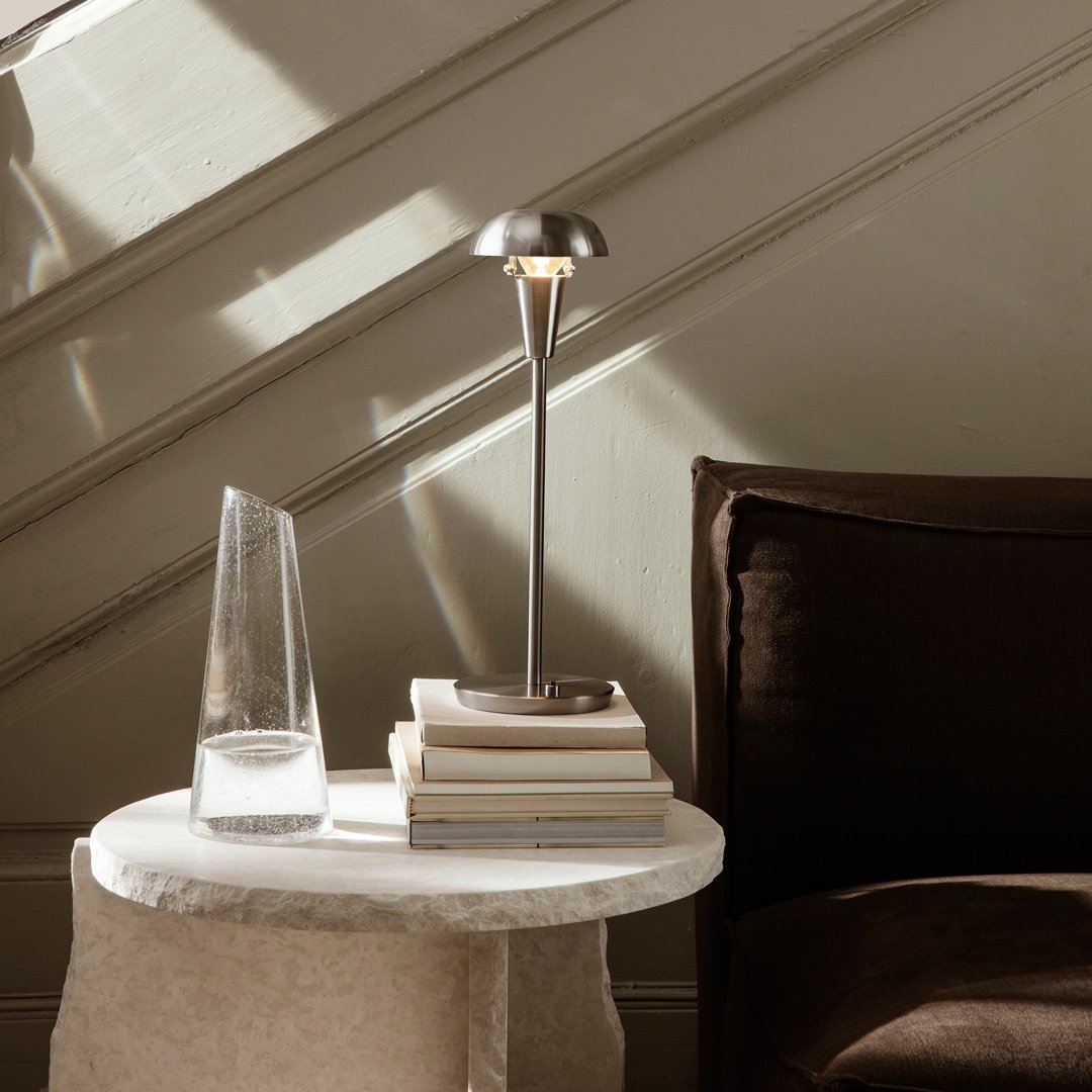 Sleek silver lamp on a marble table, complemented by earthy brown cushions and a clear glass vase, creating a chic decor.