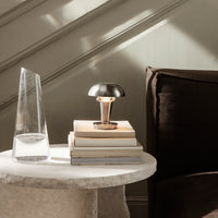 Modern black and metallic table lamp atop stacked books, grey stone table, and brown plush couch in soft light.