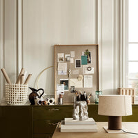 Textured cream lamp on green desk, surrounded by neutral tones and natural materials for a modern aesthetic.