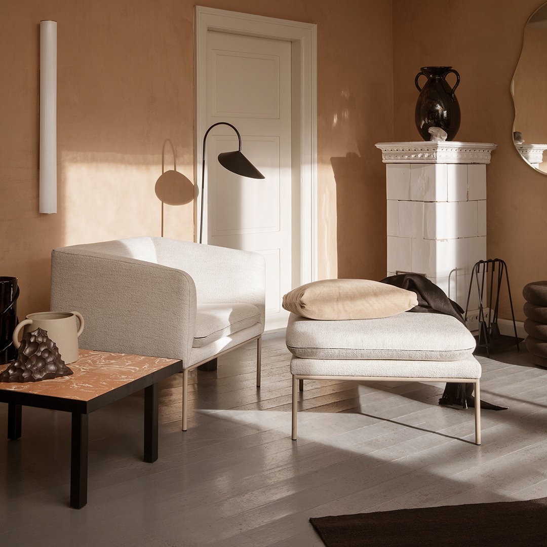 Neutral-colored chairs and ottoman with a textured cushion, set against warm beige walls and a light gray floor.