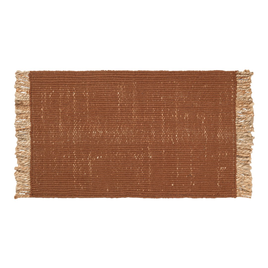 Rust-colored woven rug with fringe edges, featuring a textured, subtle pattern. Perfect for warm home decor.
