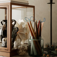 "Colorful tapered candles in a glass jar, showcasing warm tones of brown, cream, and teal against a neutral backdrop."