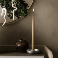 Tall amber candle in silver holder, dark ceramic vase, white decor accents, and rich earthy tones.