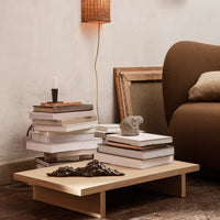 Light wooden coffee table with stacked white books and a decorative dark sculpture against a warm, neutral backdrop.