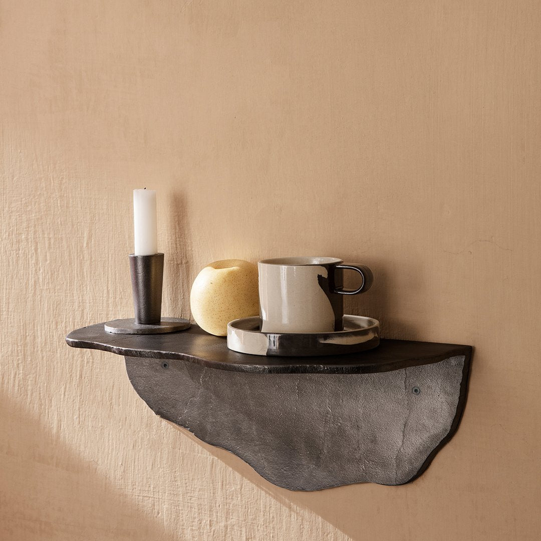Black shelf with natural texture, featuring a white candle, yellow apple, and a striped black-and-white cup and saucer.