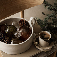 "Muted earth tones in a bowl with glass ornaments, pinecones, and a cup featuring a soft, neutral color palette."