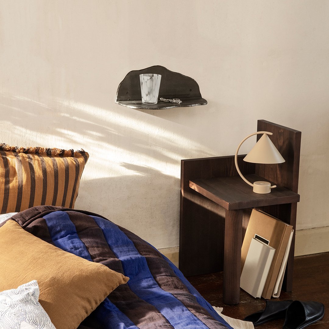 "Textured black cap above a wooden nightstand, complemented by blue and brown striped bedding and a beige lamp."