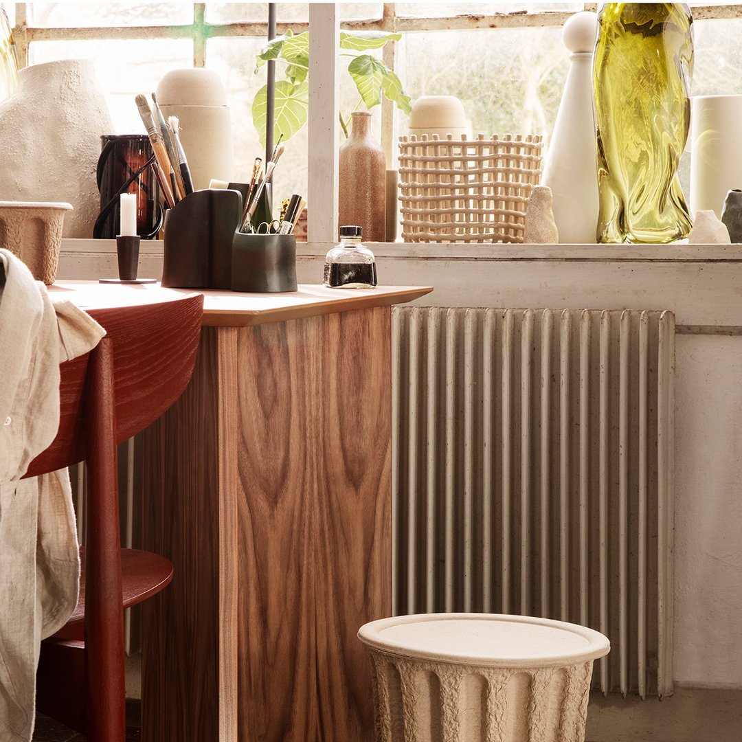 Wooden bar with a rich walnut finish, a textured cream stool, and various green and amber decorative items.