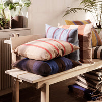 Colorful cushions featuring stripes in beige, blue, brown, and terracotta arranged on a wooden bench.