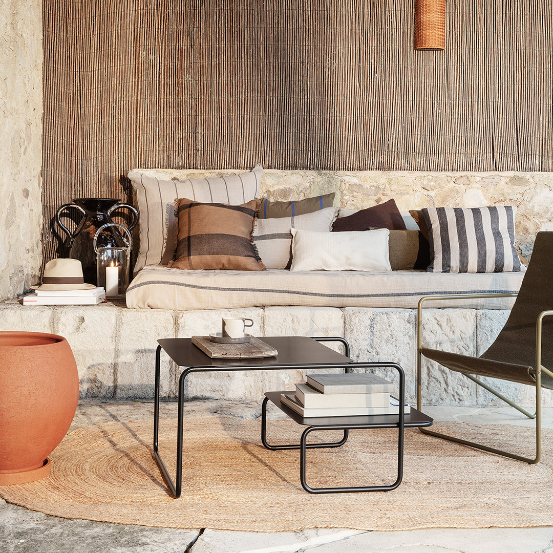 Neutral tones with striped and solid patterns on pillows; earthy terracotta vase and black metal coffee table.