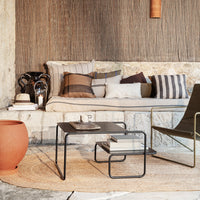 Neutral tones with striped and solid patterns on pillows; earthy terracotta vase and black metal coffee table.