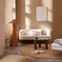 Neutral beige walls, soft white sofa, textured brown lamp, round natural fiber rug, and subtle pastel accents create a calm ambiance.