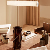 Modern, minimalist table lamp with a smooth white cylindrical shade; rich brown glass vase adds contrast to warm tones.