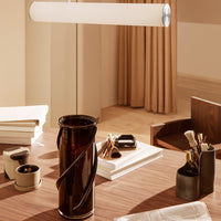 "Amber vase with a spiral pattern on a warm-toned wooden desk, surrounded by neutral-colored decor."