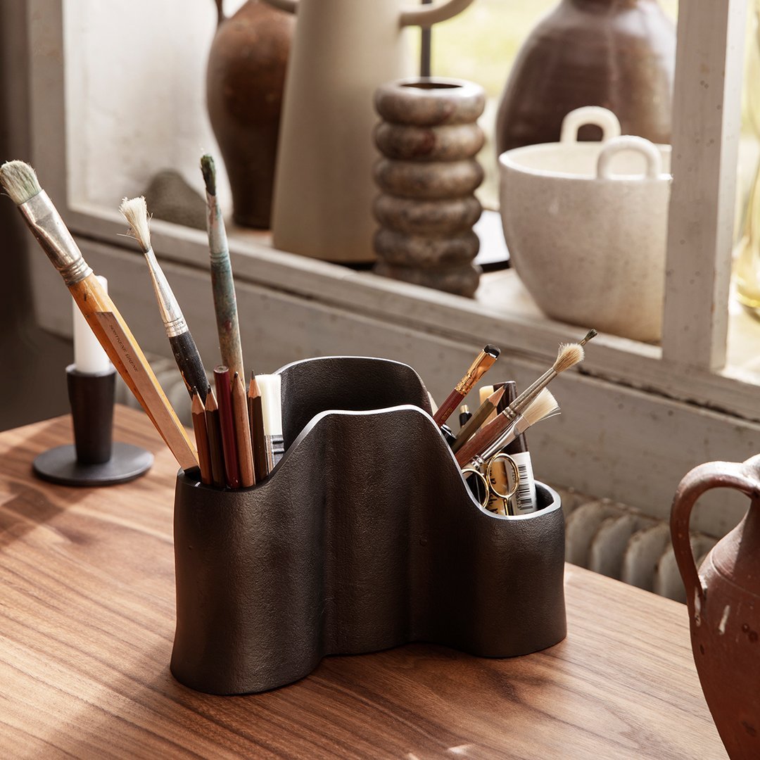 Black wavy pen holder with a glossy finish, featuring a mix of natural wood and metallic-colored writing tools.