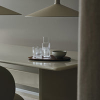 Minimalist table setting with clear glasses, a bowl, and a brown wood tray under soft, neutral lighting.