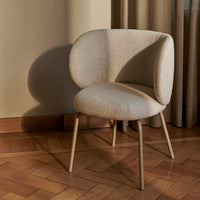 Beige upholstered chair with a curved back and light brown wooden legs, featuring a soft, textured fabric.