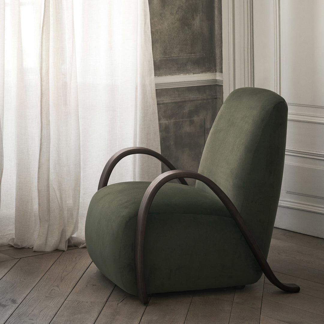 Green upholstered chair with smooth curves and dark wood accents, set against a light, neutral background.