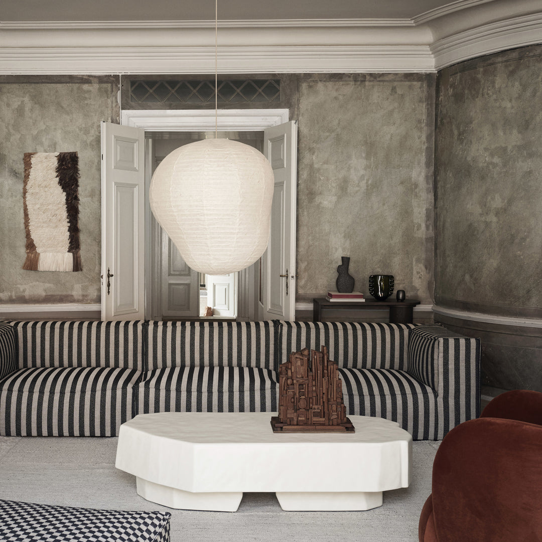 Striped blue and white sofa with a beige pendant light against a textured gray wall and dark wood accents.