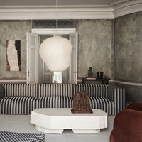 Striped blue and white sofa with a beige pendant light against a textured gray wall and dark wood accents.