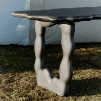 Stylish black table with a textured, wavy top and uniquely shaped gray legs on a natural grass background.
