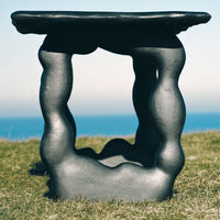 Unique black sculptural table with organic, curved edges set against a natural outdoor backdrop.