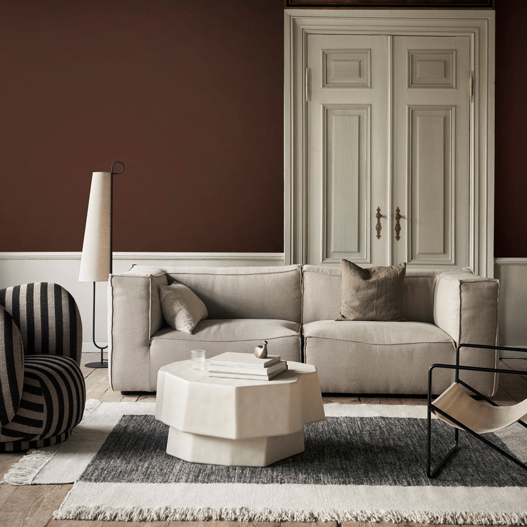 Neutral beige sofa with textured cushions, black and white striped chair, and a geometric cream coffee table on a gray rug.