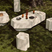 Outdoor table set featuring a smooth, white finish and organic shapes, complemented by dark and amber-colored tableware.
