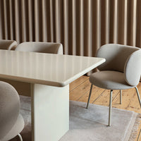 Beige and cream dining table with rounded edges, surrounded by soft, textured beige chairs on a light rug.