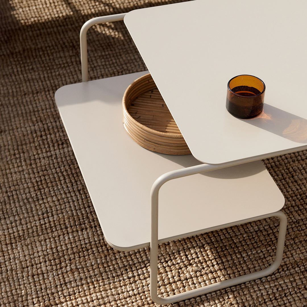 Minimalist white coffee table with smooth surfaces and a light wood tray, set on a textured natural fiber rug.