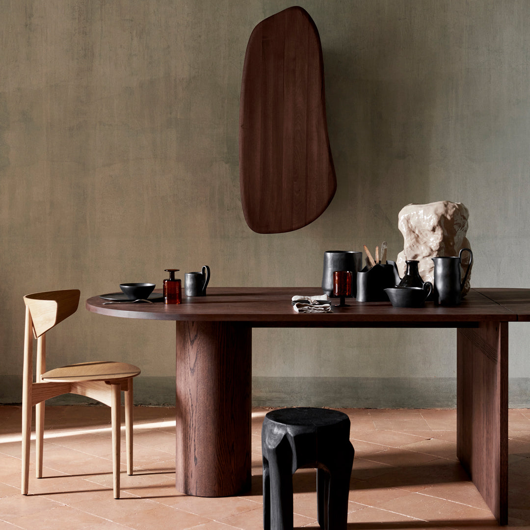 Elegant wooden dining table with brown tones, paired with a light wooden chair and black ceramic decor. Minimalistic and modern design.