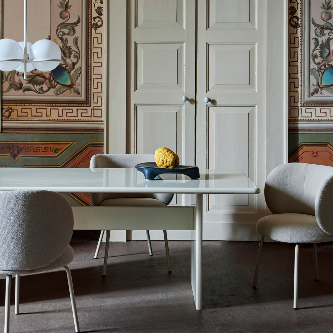 Elegant modern dining table with white finish, paired with soft gray chairs against a decorative patterned wall.