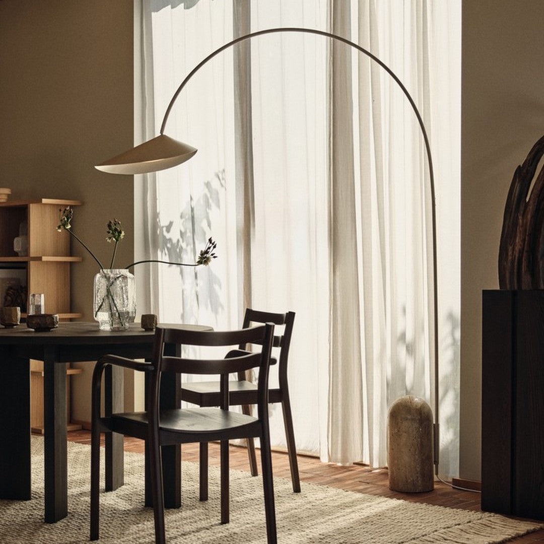 Modern black chair with sleek lines, warm neutral walls, and natural light illuminating soft white curtains and earthy textures.