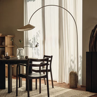 Modern black chair with sleek lines, warm neutral walls, and natural light illuminating soft white curtains and earthy textures.