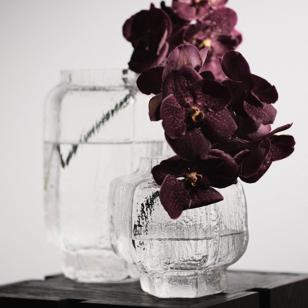 Clear textured glass vases with deep purple orchids, showcasing a modern design and elegant color contrast.