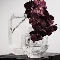 Clear textured glass vases with deep purple orchids, showcasing a modern design and elegant color contrast.