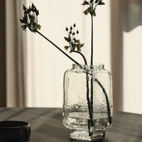 Textured clear glass vase with subtle ripples, showcasing delicate green stems and muted floral tones.