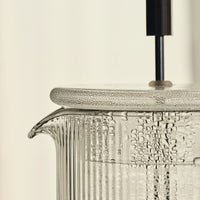Clear glass pitcher with textured ribbed pattern and sleek black handle, showcasing bubbles in the water inside.