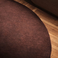 Round brown rug with a soft, textured surface, complementing wooden floors with warm tones.