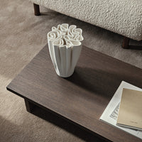 White sculptural vase with a textured pattern on a dark wooden table, complemented by neutral-toned decor.