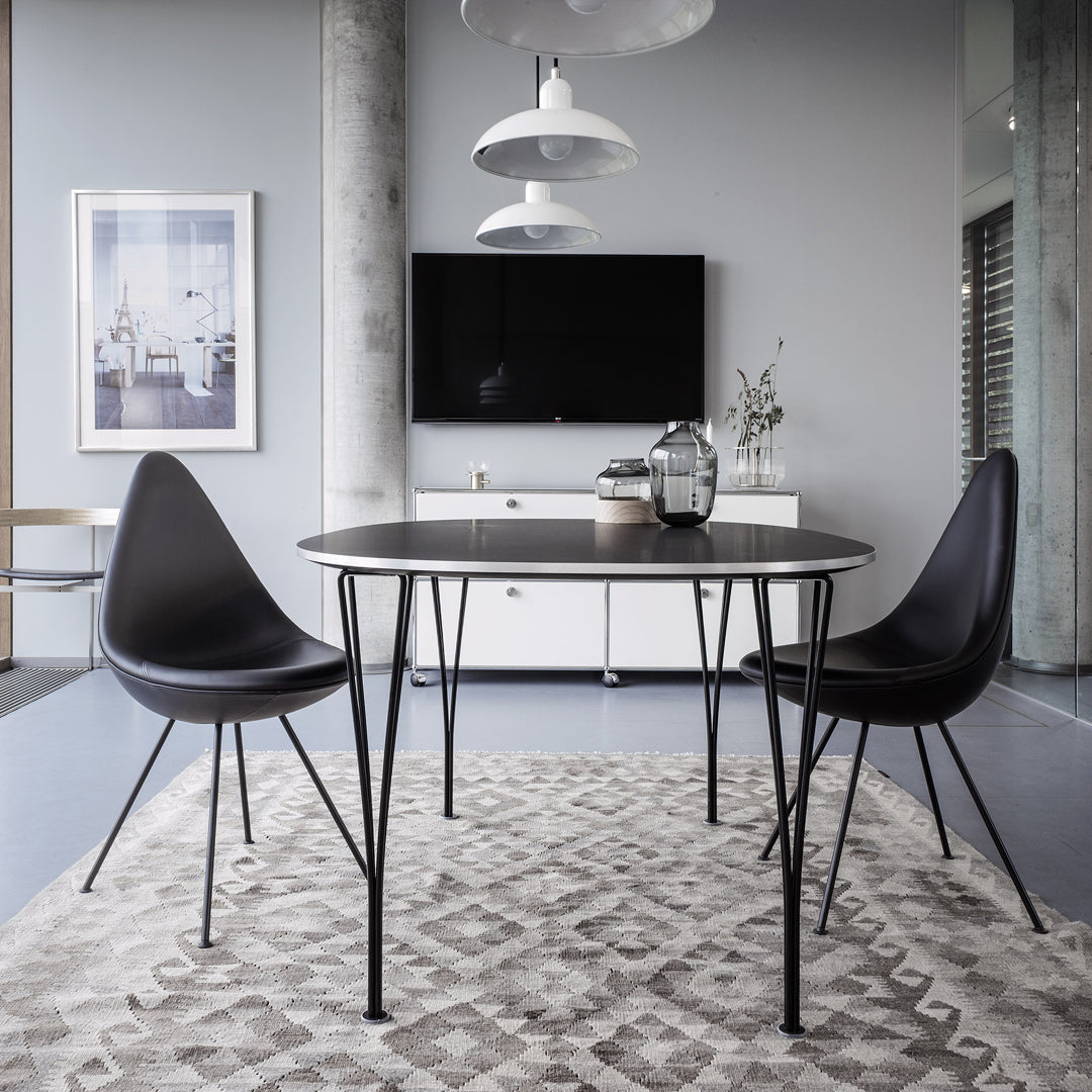 Black round dining table and chairs on a textured beige rug, set against a modern grey backdrop.