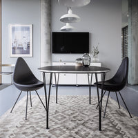 Black round dining table and chairs on a textured beige rug, set against a modern grey backdrop.