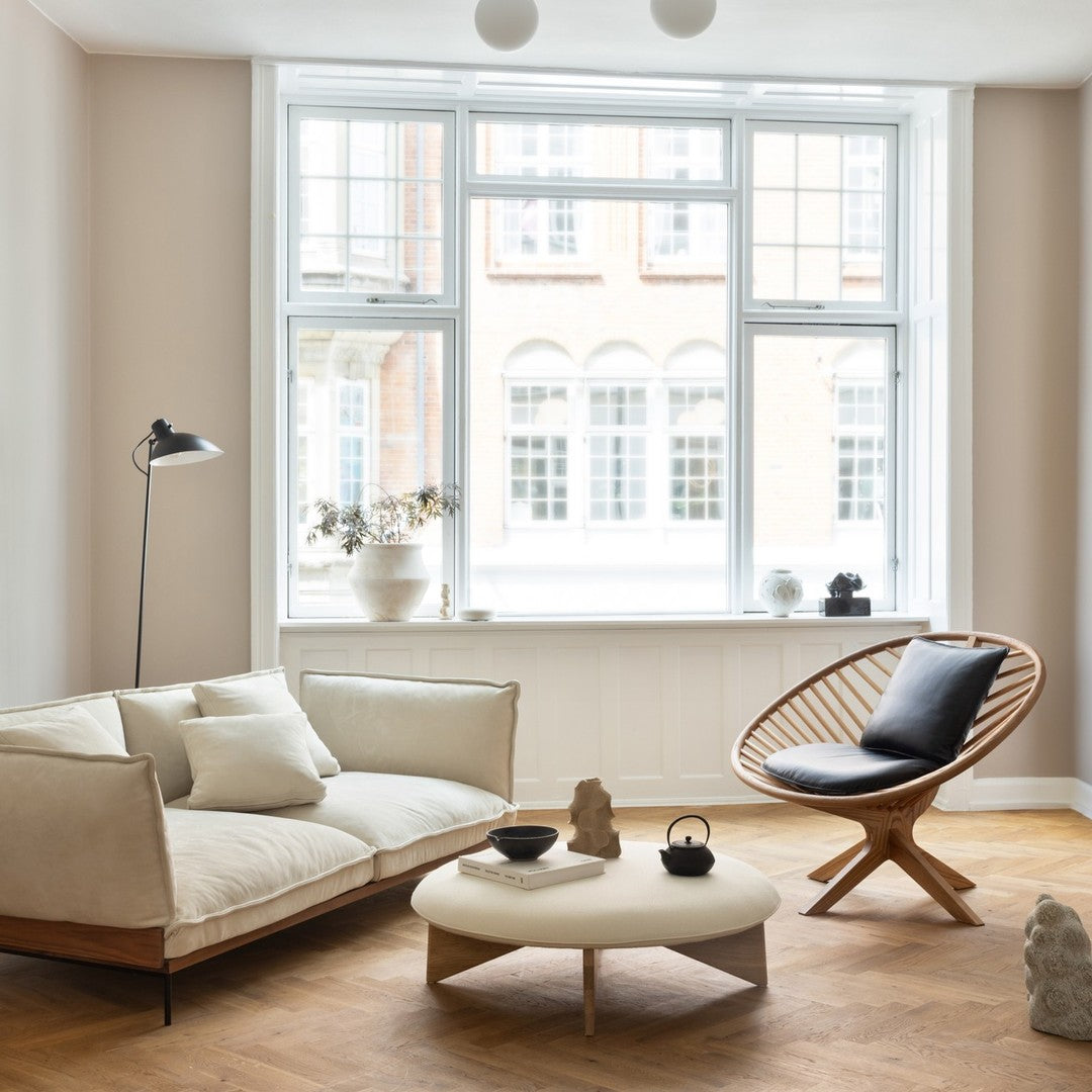 Light beige sofa with cream cushions, natural wood accents, and a minimalist black and white chair in a bright, airy room.