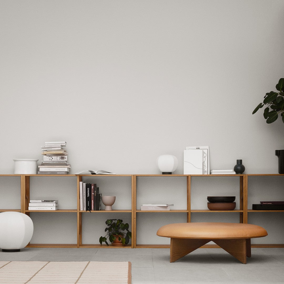Modern wooden shelf with light oak finish, featuring white and black decor, and green plants against a neutral wall.