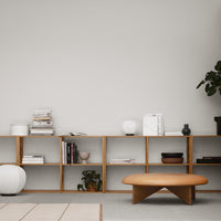 Modern wooden shelf with light oak finish, featuring white and black decor, and green plants against a neutral wall.
