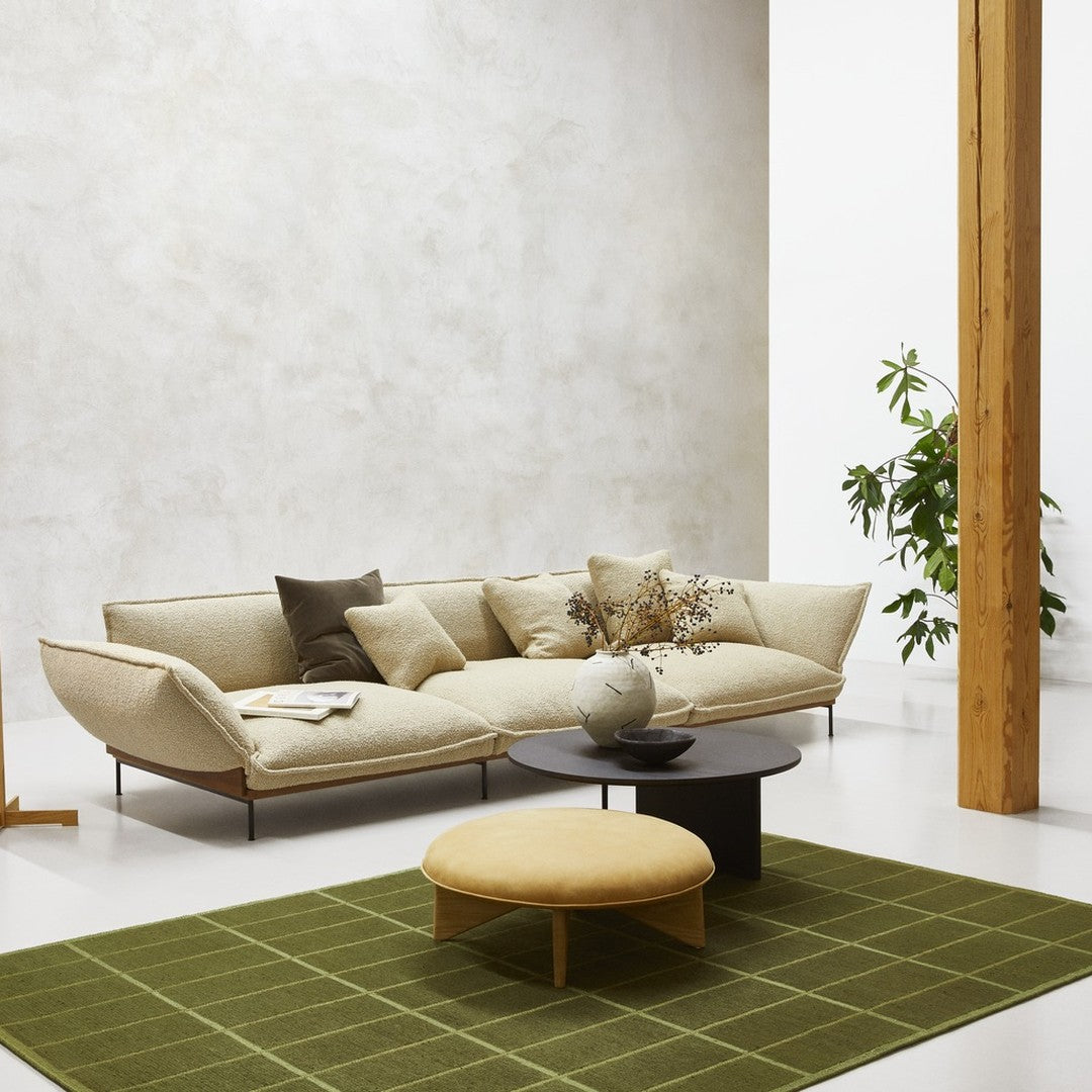 Beige sofa with neutral cushions, round yellow ottoman, and a green grid-pattern rug on a light floor.