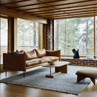 Mid-century modern living room featuring a brown leather sofa, light gray rug, and natural wood accents.